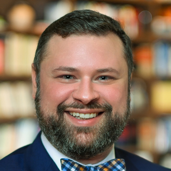 Ethan Hussong smiling in a library, wearing a navy suit and patterned bow tie.